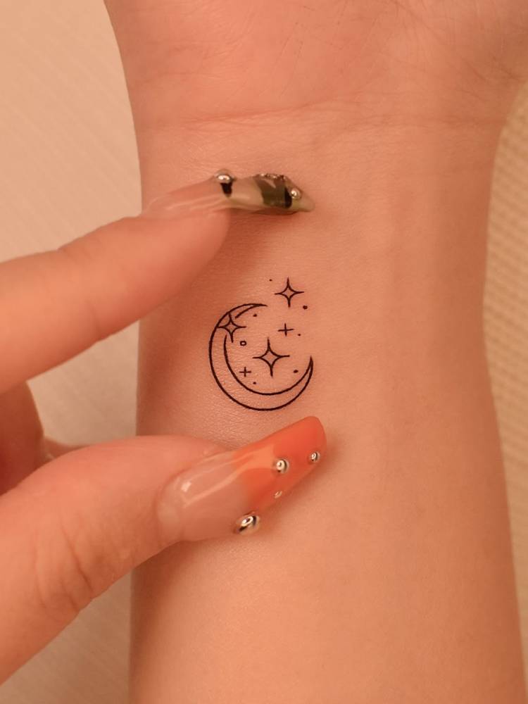 Moon and stars tattoo in minimalistic style placed on the wrist.