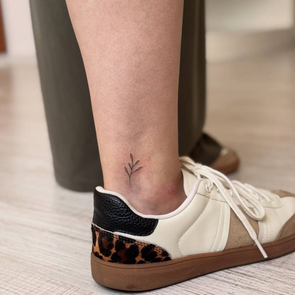 Tiny fine line style sprout tattoo located on the ankle.