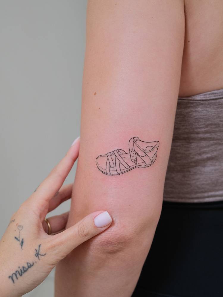 Fine line sandal tattoo located on  the tricep.