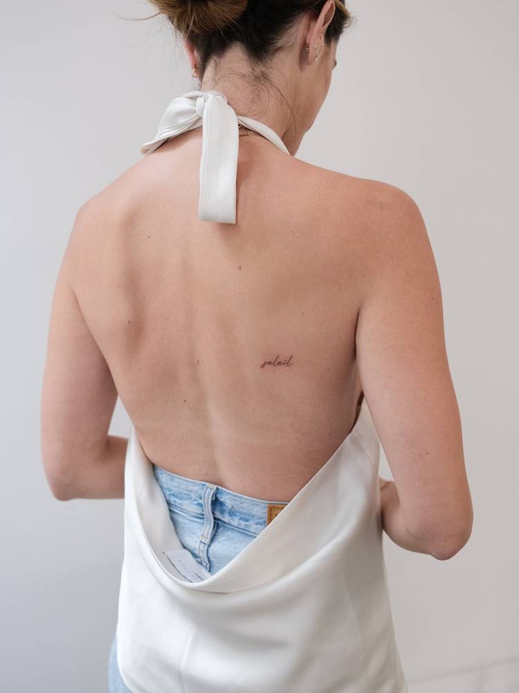 Handwritten font word "soleil" tattoo located on the back.