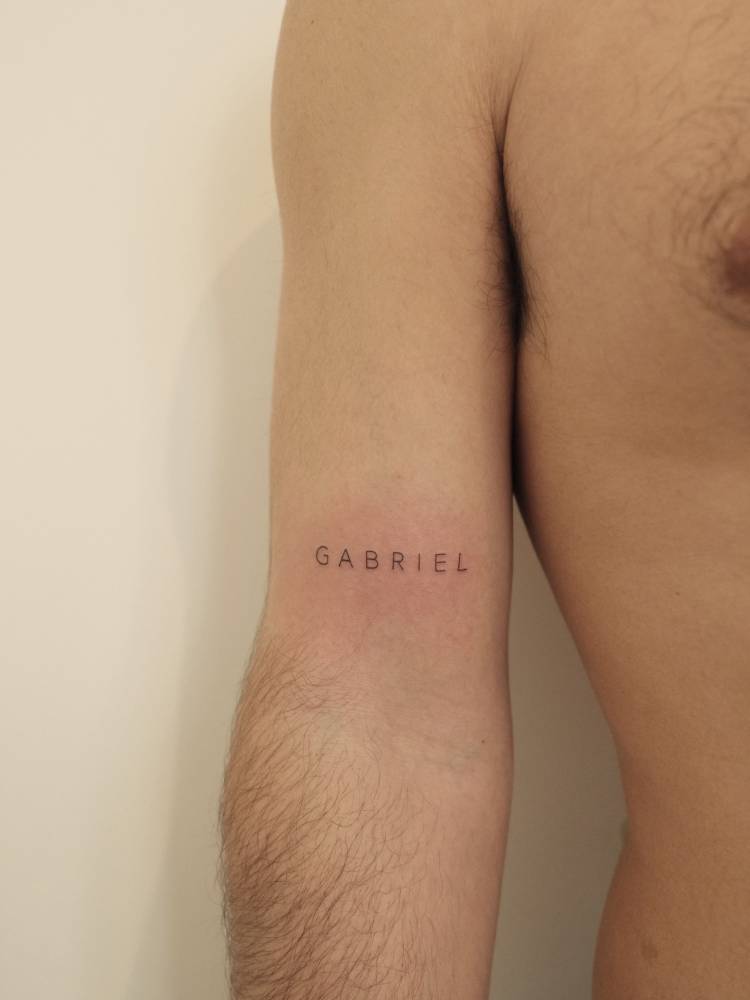 Lettering tattoo of the name "Gabriel" located on the bicep.