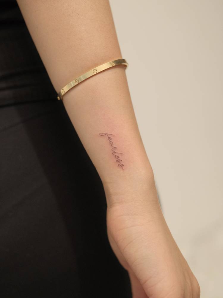 Handwritten font word "fearless" tattoo located on the wrist.