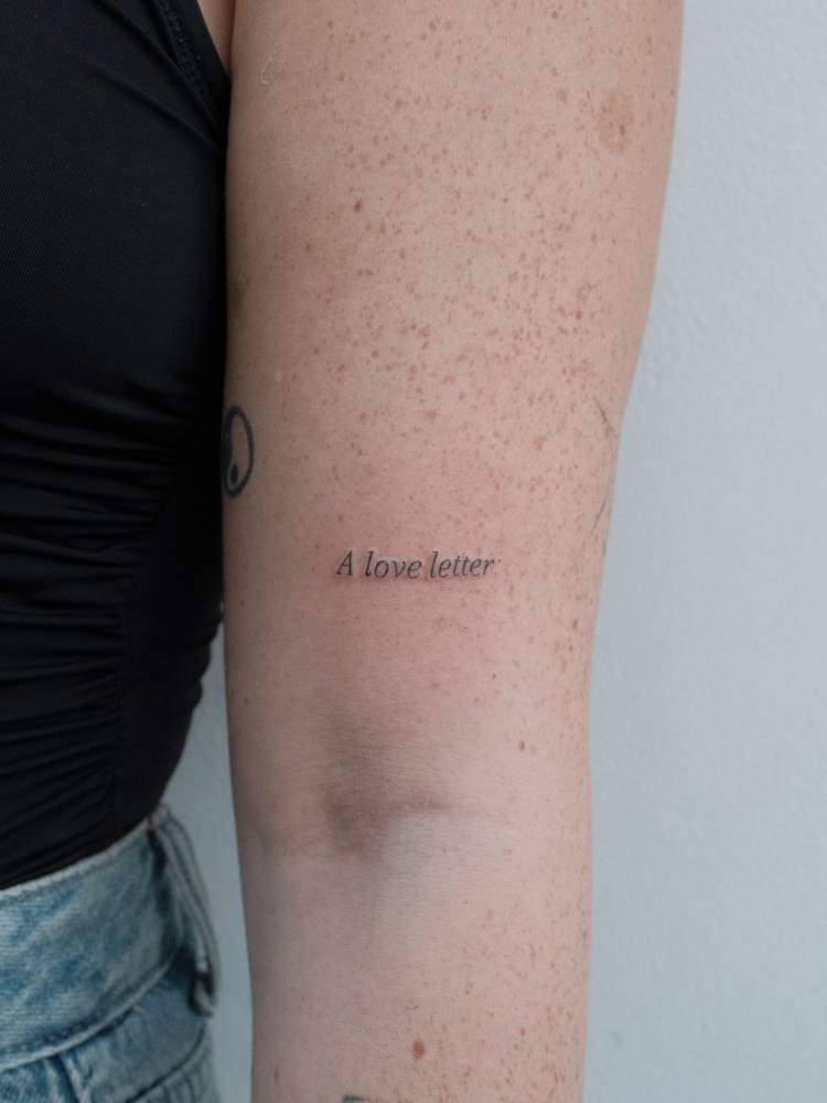 "A love letter" tattoo in serif font located on the upper arm.