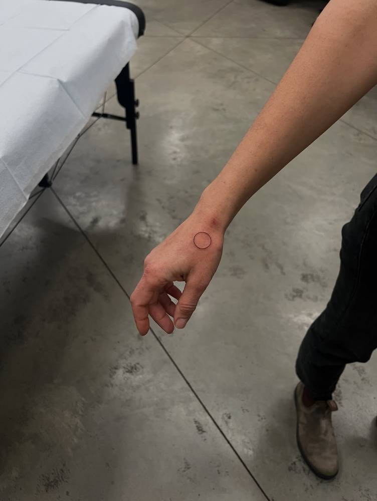 Tiny minimalistic circle tattoo located on the hand.