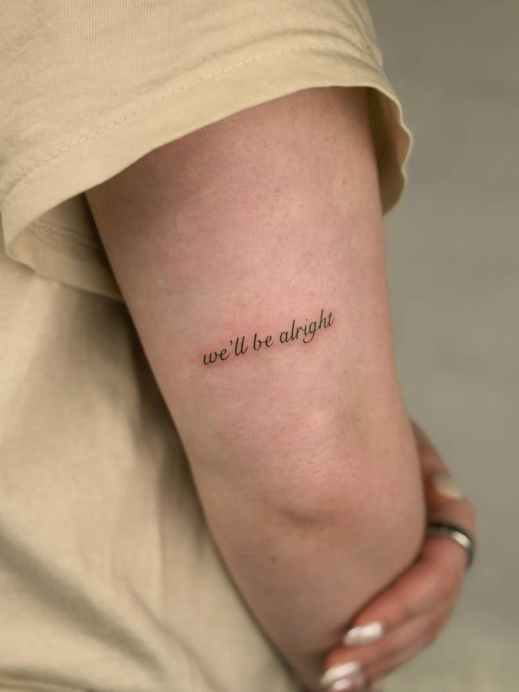 "We'll be alright" lettering tattoo placed on the tricep.