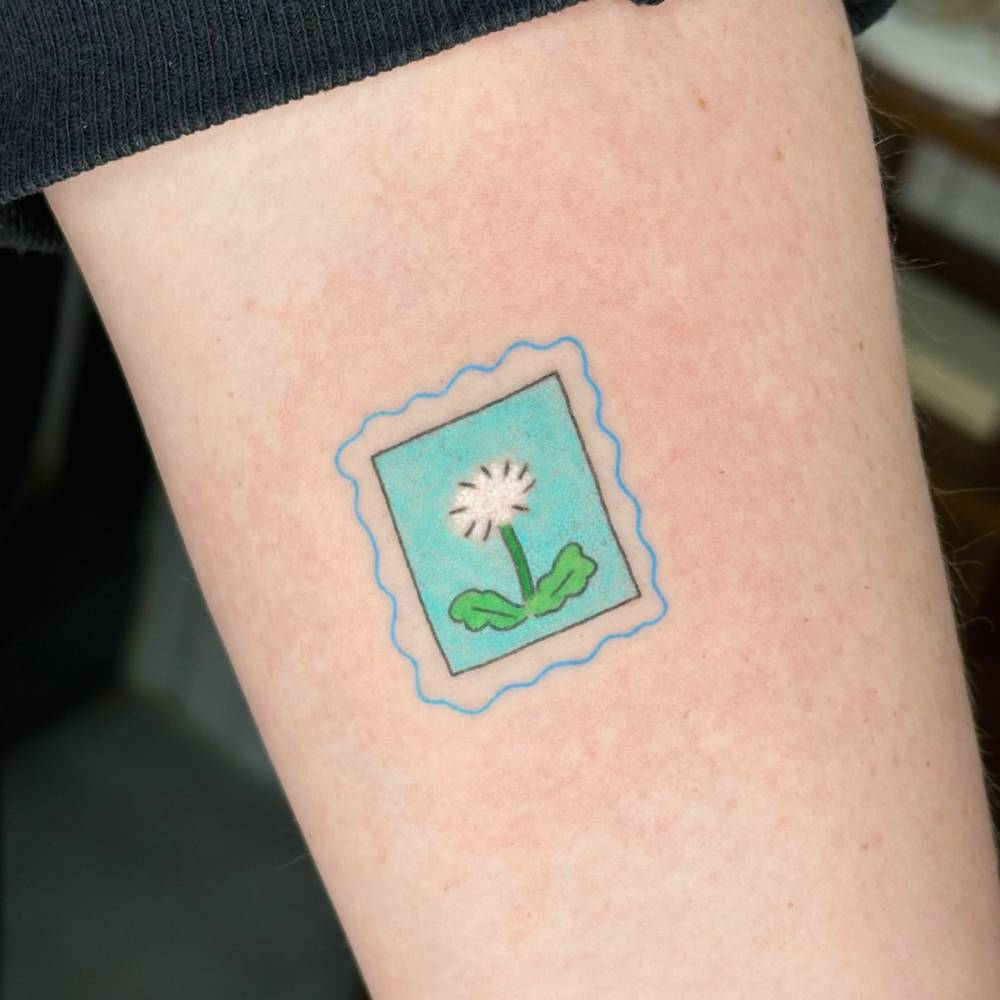 Dandelion stamp tattoo in cartoon style located on the inner forearm.