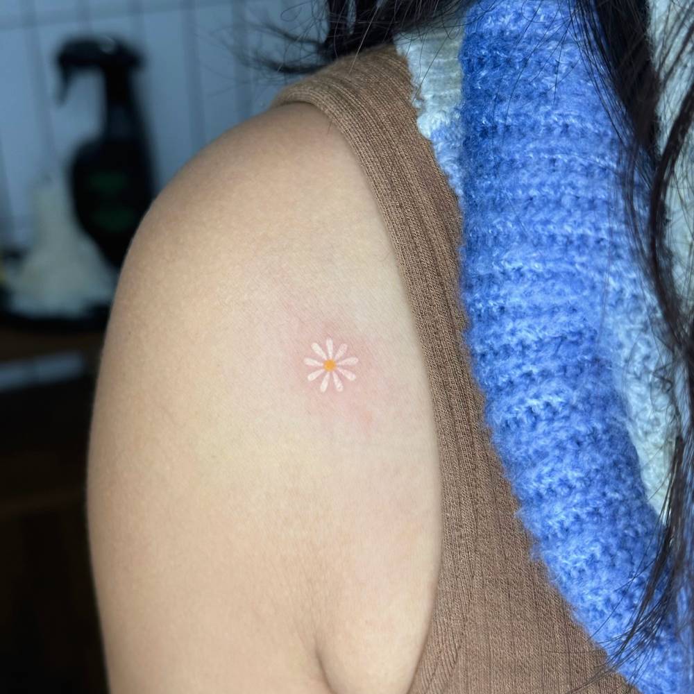 Hand poked daisy flower tattoo located on the shoulder.