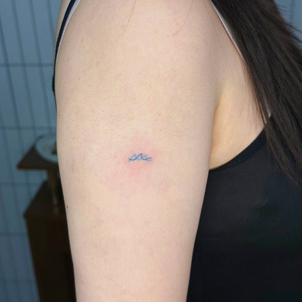 Tiny waves tattoo in minimalistic style hand poked on the upper arm.