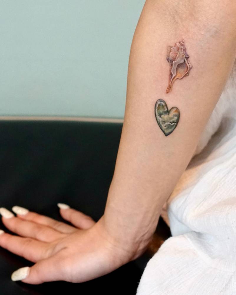 Tulip shell and pebble heart tattoo located on the inner forearm.