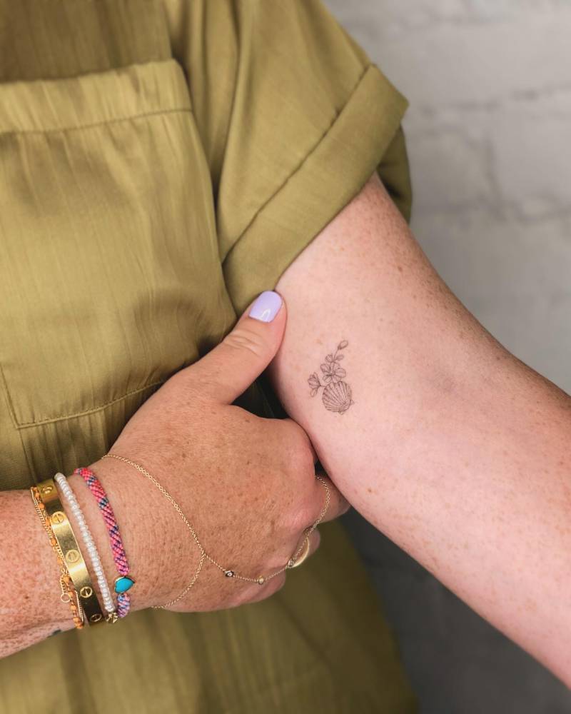 Shell and flowers tattoo in fine line style located on the inner arm.