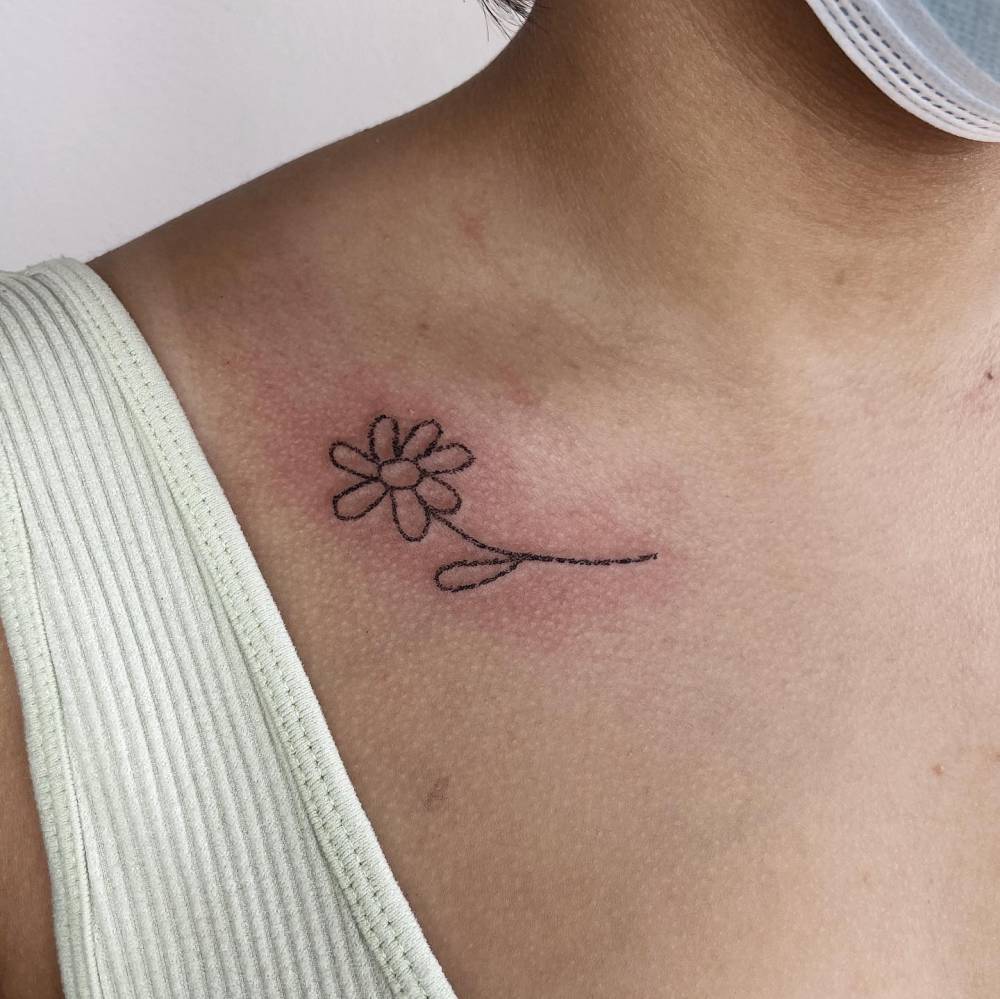 Crayon flower tattoo located on the collarbone, minimalistic style.