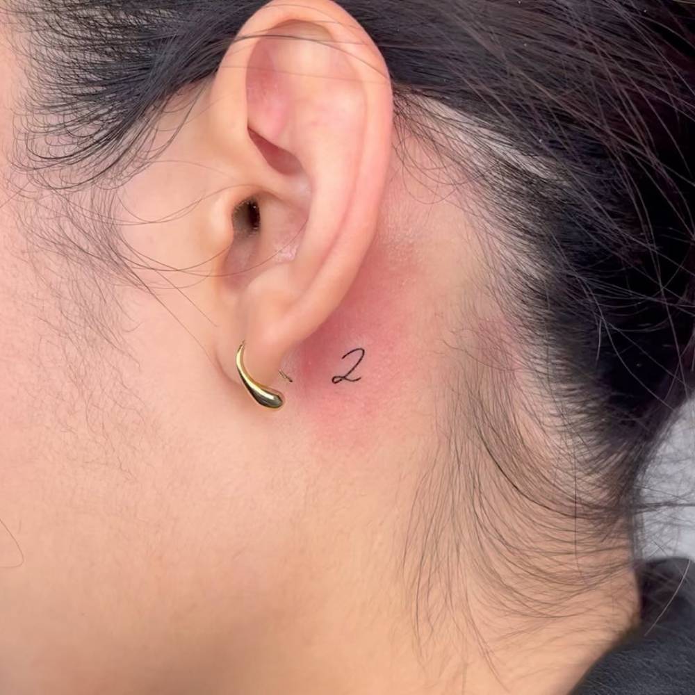 Tiny tattoo of the number "2" located behind the ear.