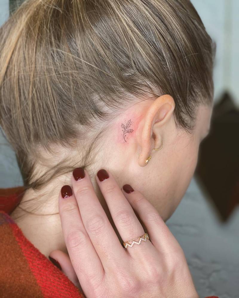 Fine line style holly tattoo located behind the ear.