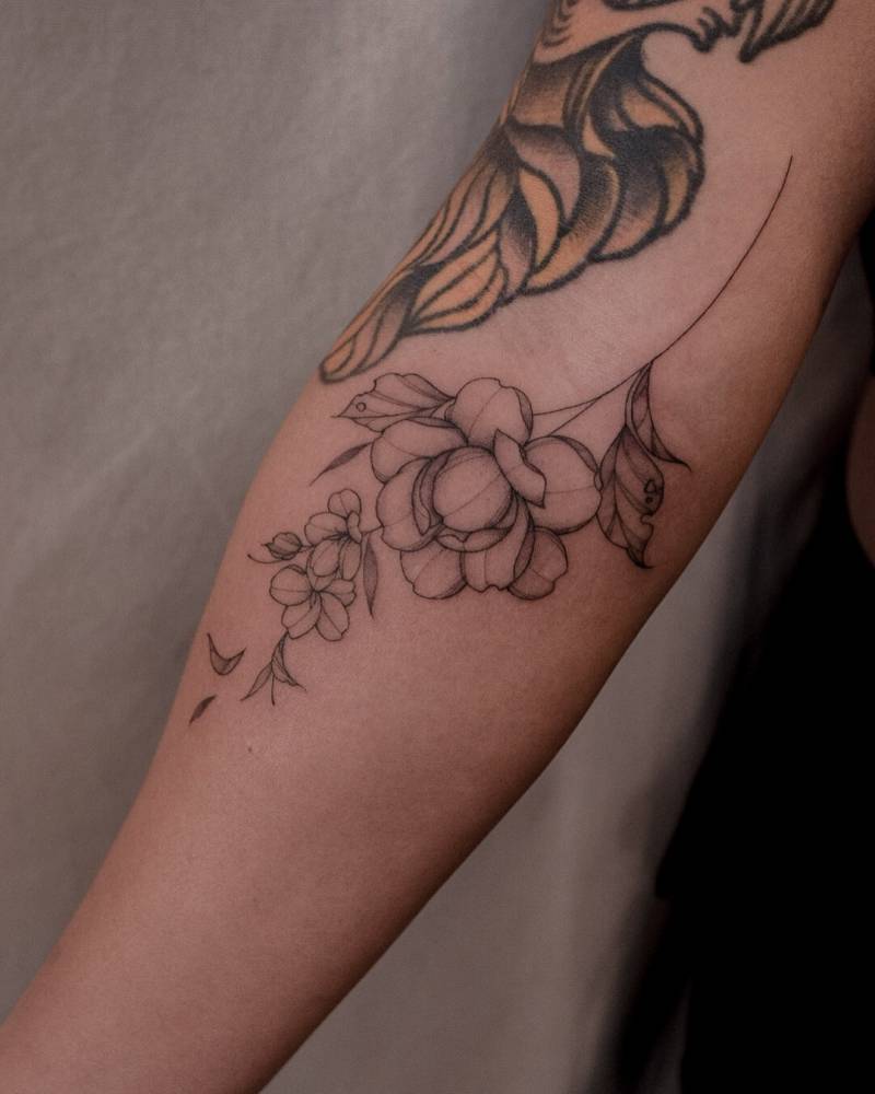 Illustrative style peony and cherry blossom tattoo located on the inner forearm.