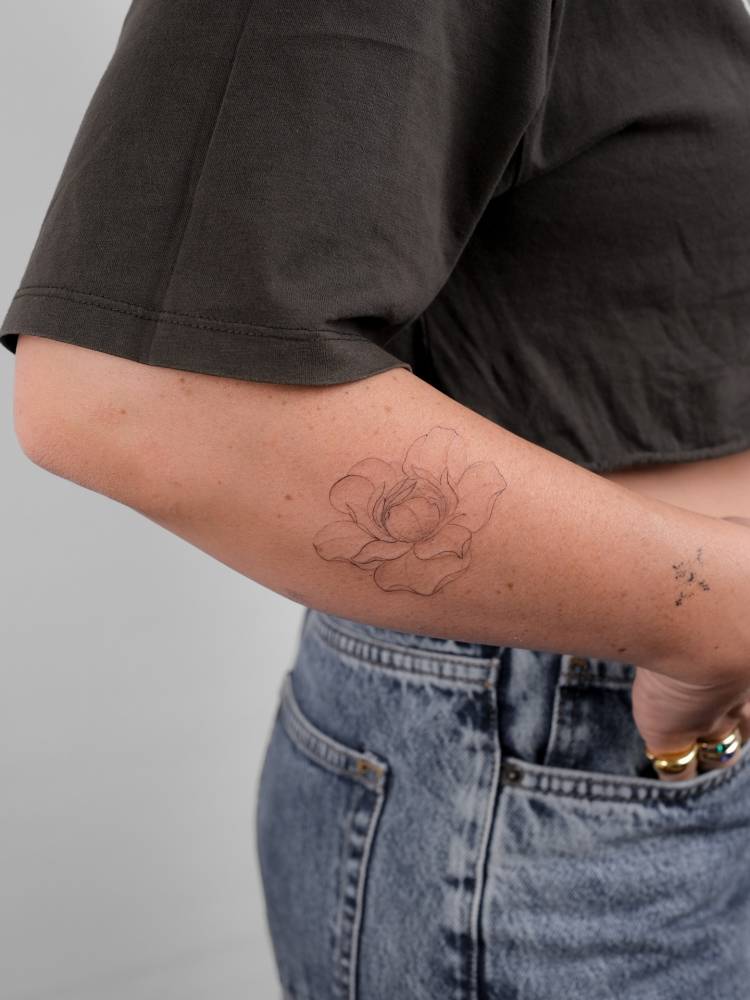 Peony flower tattoo located on the forearm, done in fine line style.