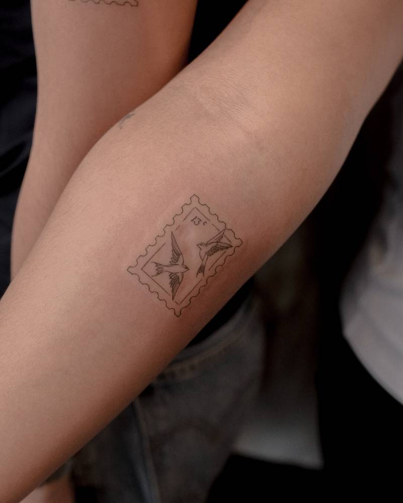 Fine line style swallow stamp tattoo located on the inner forearm.