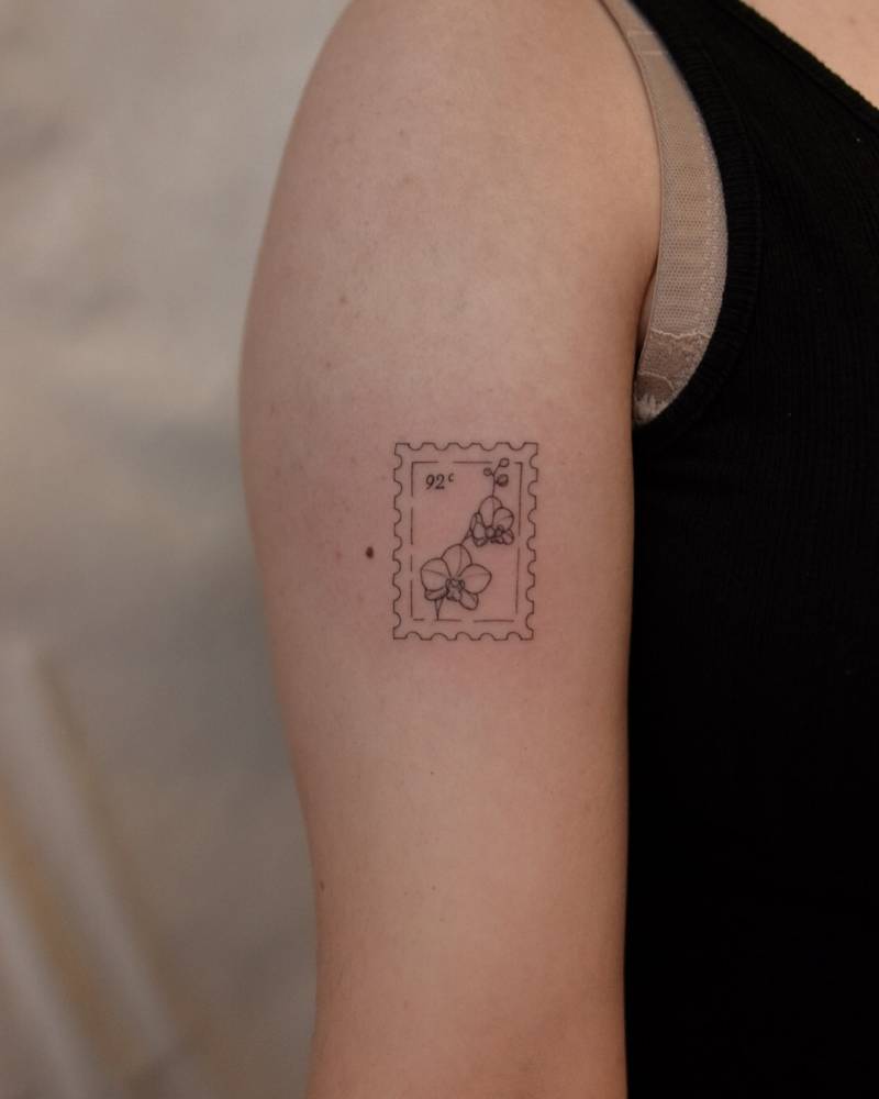 Orchid stamp tattoo in fine line style located on the upper arm.