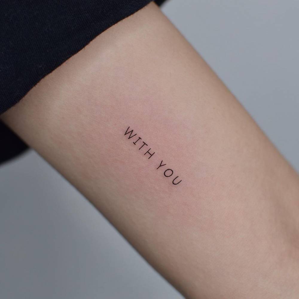 "With you" lettering tattoo on the inner arm