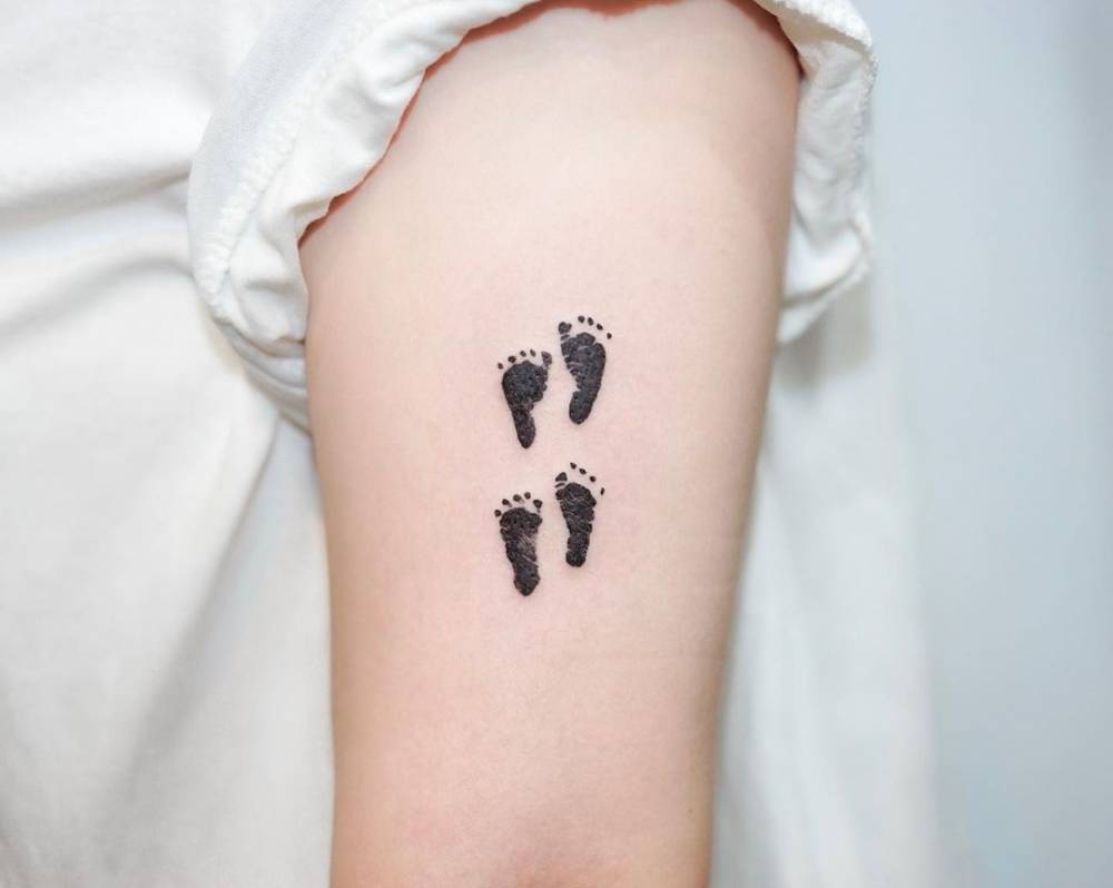 Watercolor footprints tattoo on the upper arm.
