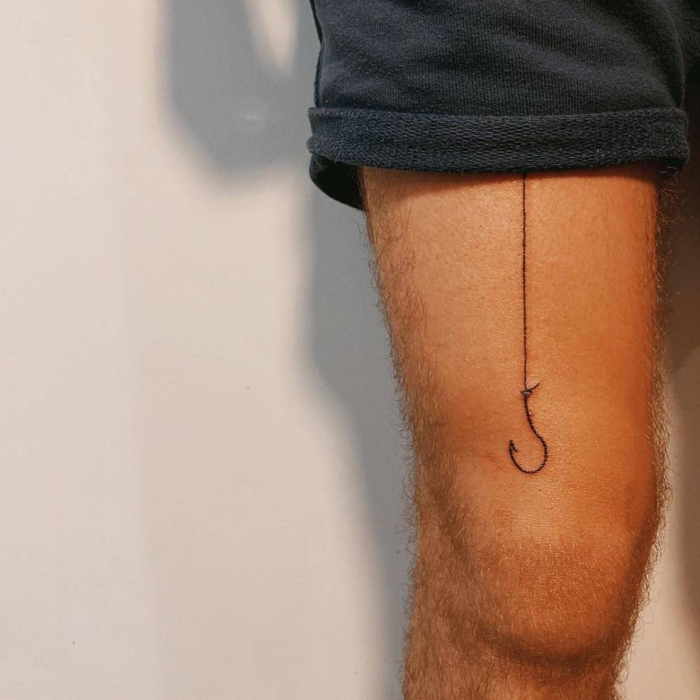 Line art fish hook tattoo on the thigh.
