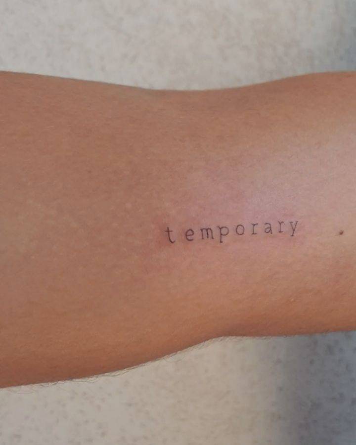 "Temporary" lettering tattoo on the elbow.