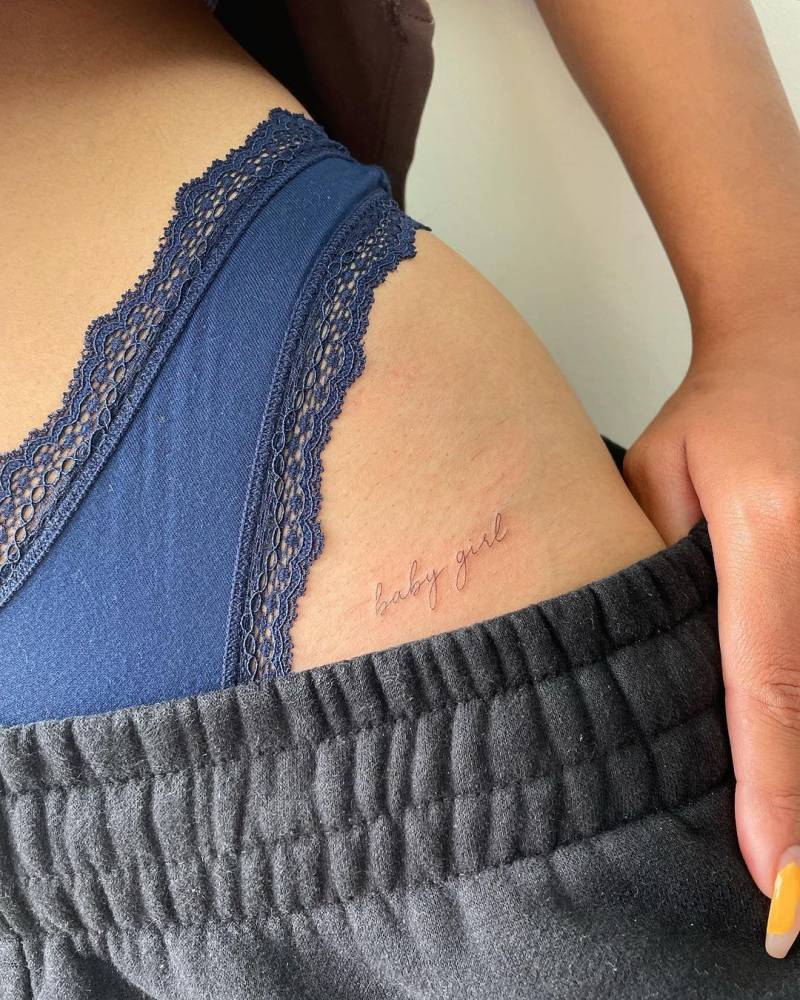 "Baby girl" lettering tattoo on the pelvis.