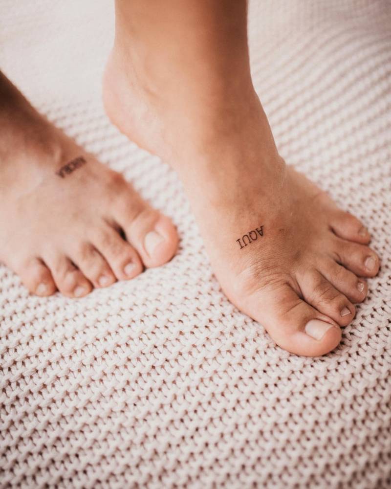 "Aquí" and "Ahora" individual matching lettering tattoo on the foot.