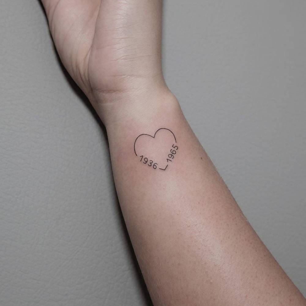 Fine line heart and birth years tattoo on the wrist.