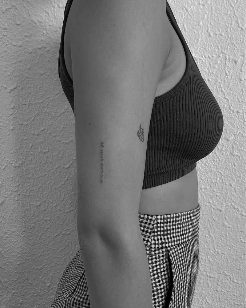 "Be your own sun" lettering tattoo on the upper arm.