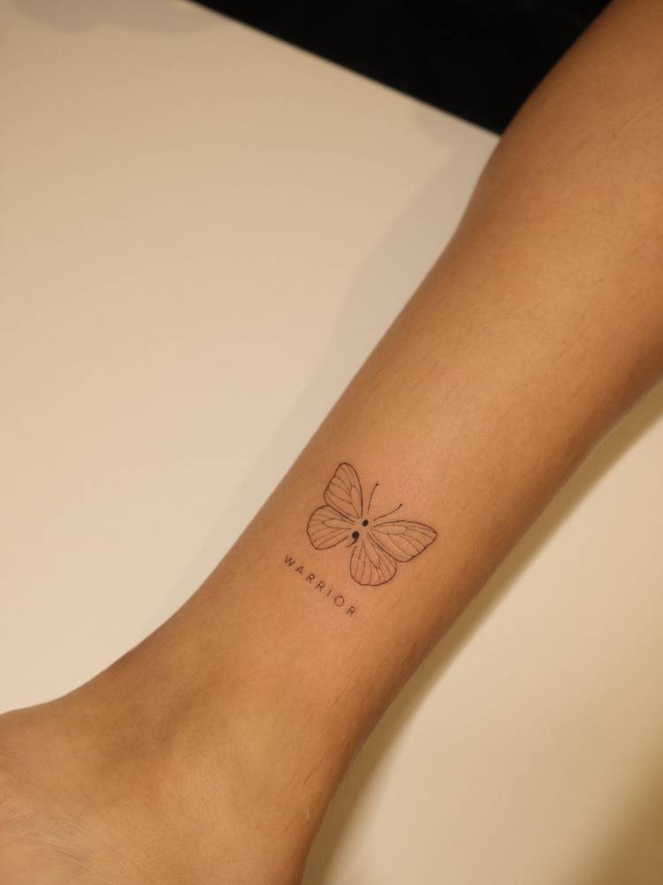 Butterfly and word "warrior" tattoo located on the ankle, fine line style.