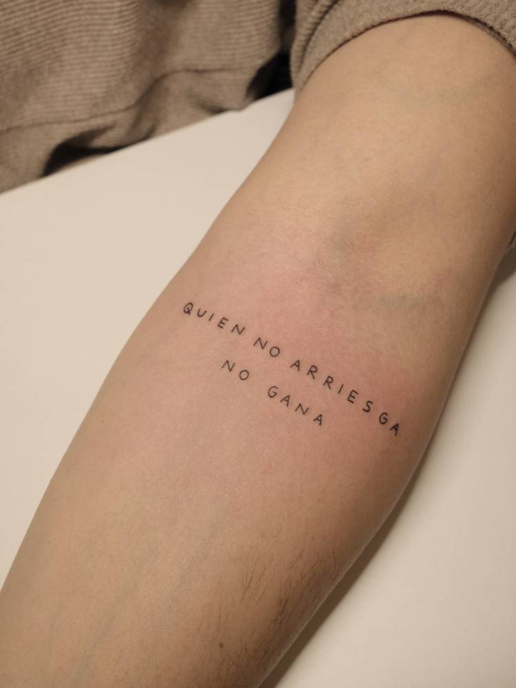 "Quien no arriesga no gana" lettering tattoo located on the inner forearm.