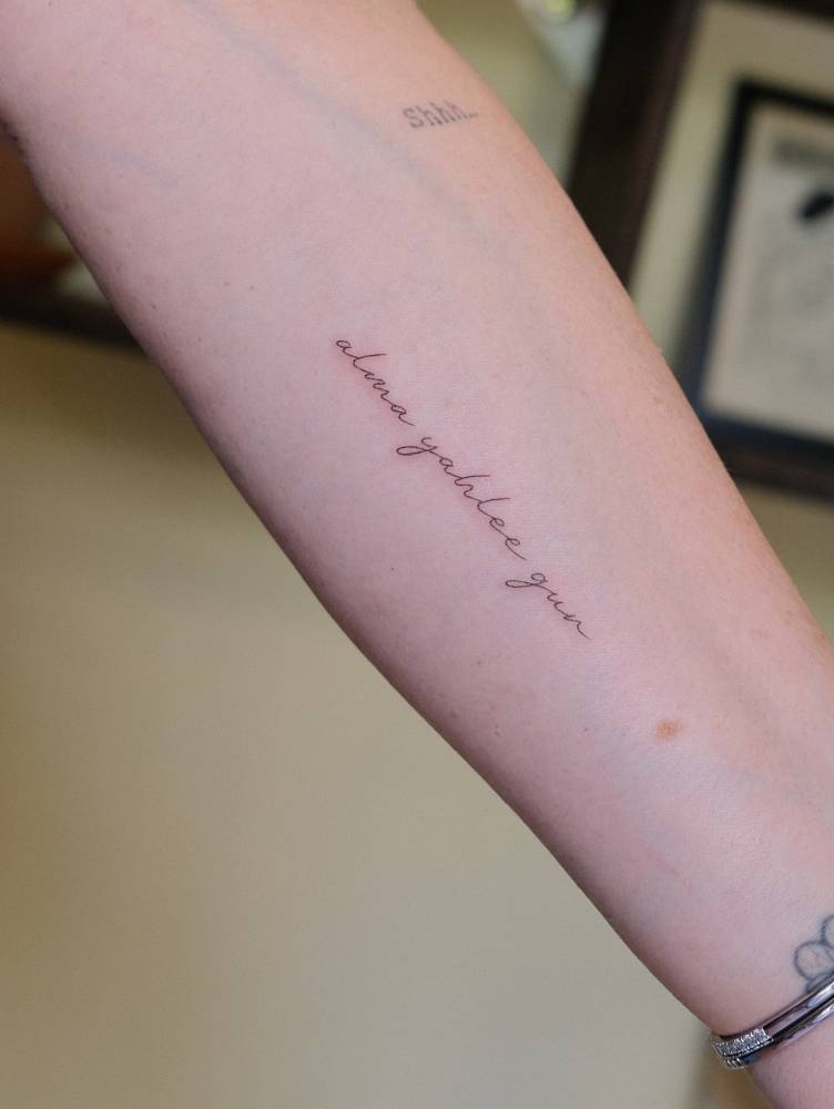 Handwritten font name tattoo located on the inner forearm.