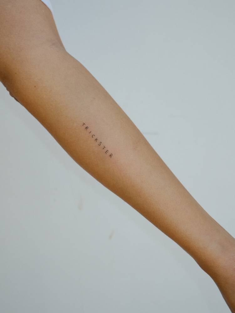 "Trickster" lettering tattoo done on the inner forearm.