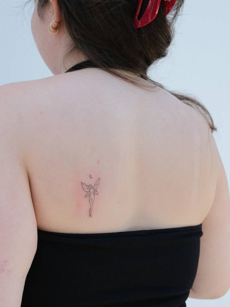 Cute fairy tattoo in fine line style placed on the shoulder blade.