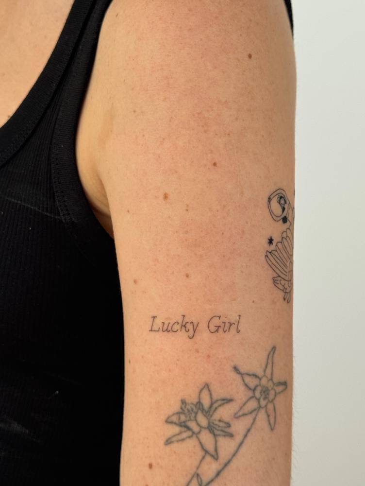"Lucky girl" lettering tattoo located on the upper arm.