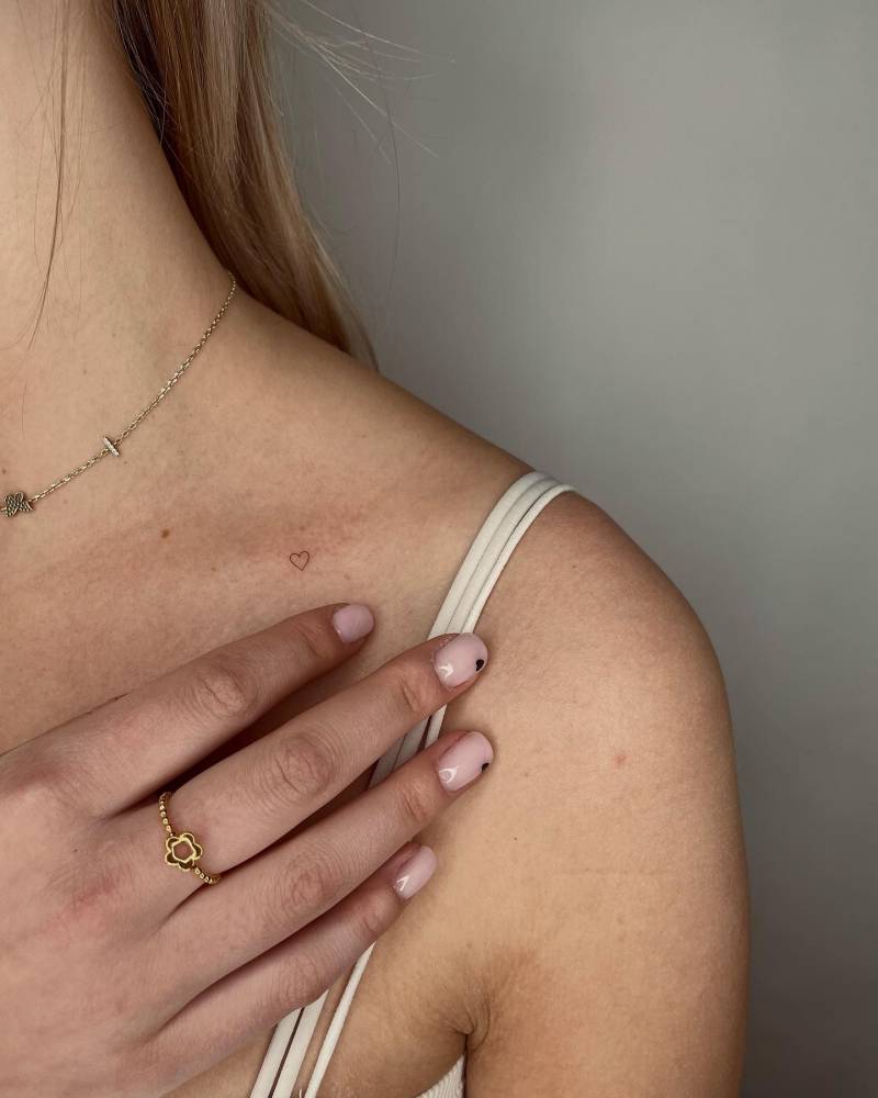 Micro heart tattoo located on the collarbone, minimalistic style.