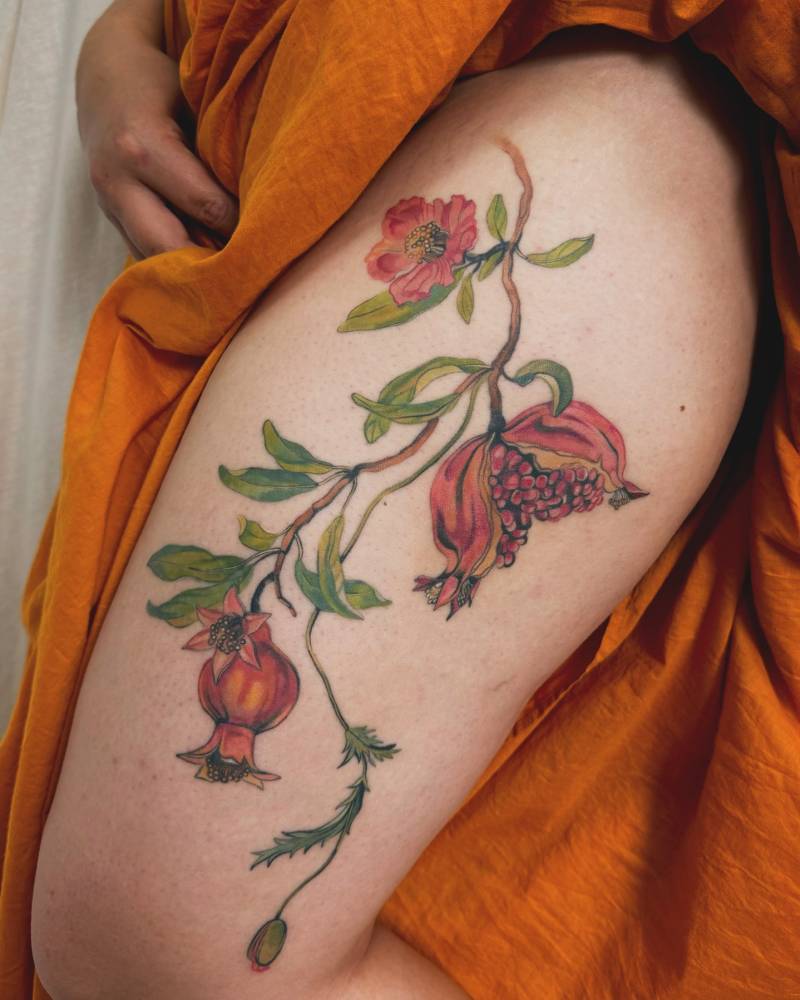 Pomegranates tattoo located on the thigh, done in watercolor style.
