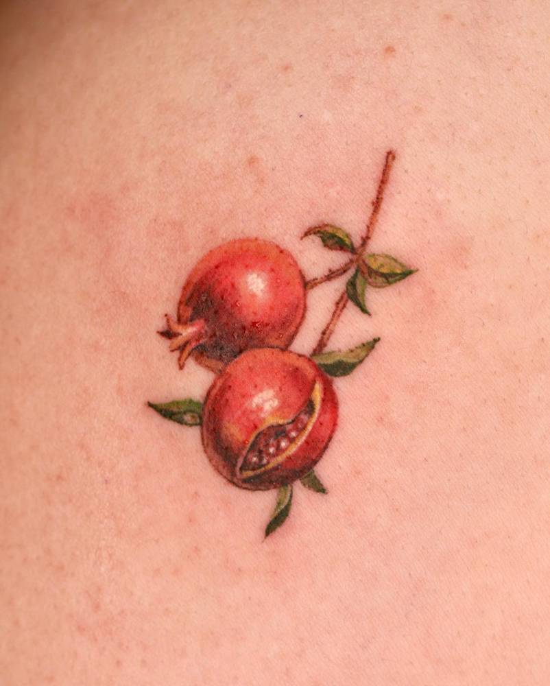 Watercolor style pomegranate tattoo located on the shoulder.