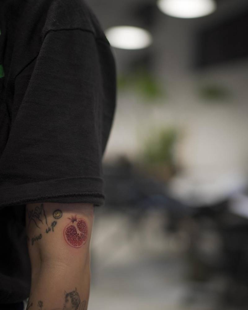 Micro-realistic style pomegranate tattoo located on the upper arm.