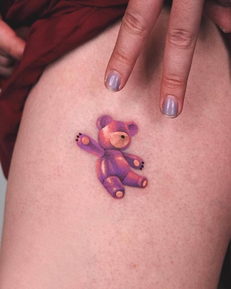 Watercolor style teddy bear tattoo located on the thigh.