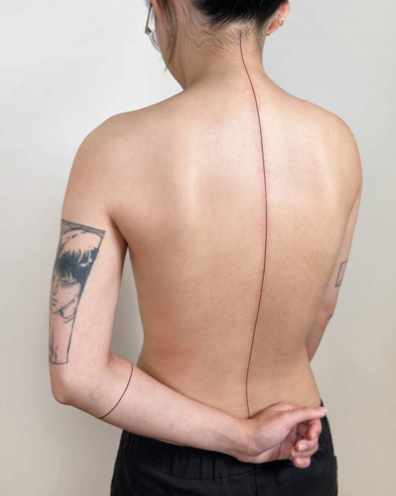 Minimalistic style line tattooed on the spine.