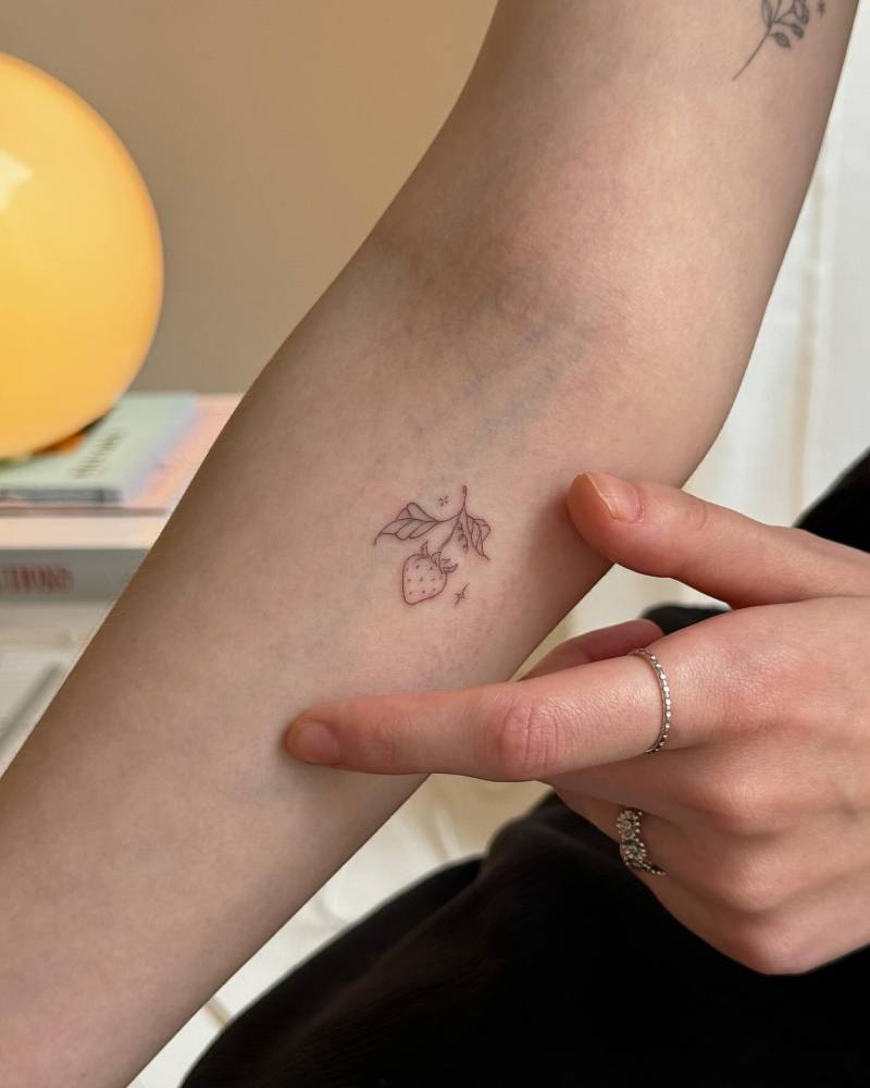 Strawberry tattoo in fine line style located on the inner forearm.