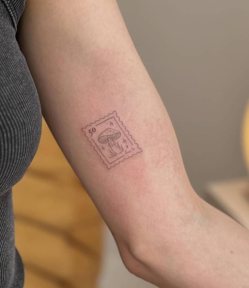Fine line style mushroom stamp tattoo placed on the inner arm.
