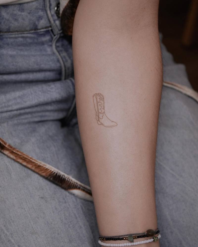 Fine line style cowboy boot tattoo located on the inner forearm.