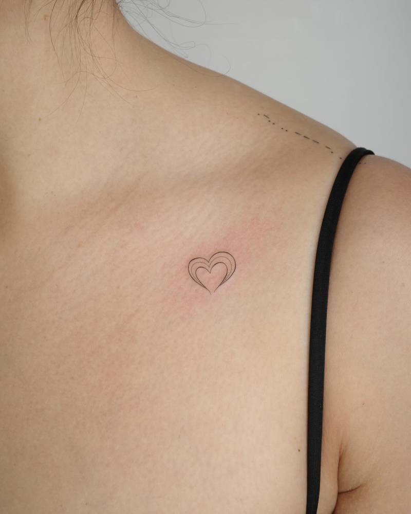 Minimalistic heart tattoo located on the collarbone, fine line style.