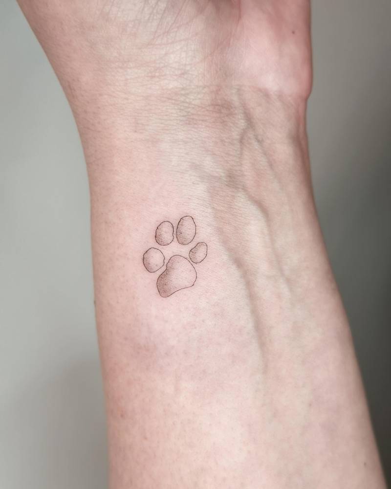 Minimalistic style dog paw print tattoo located on the wrist.