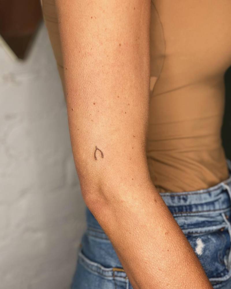 Tiny minimalistic wishbone tattoo placed on the upper arm.