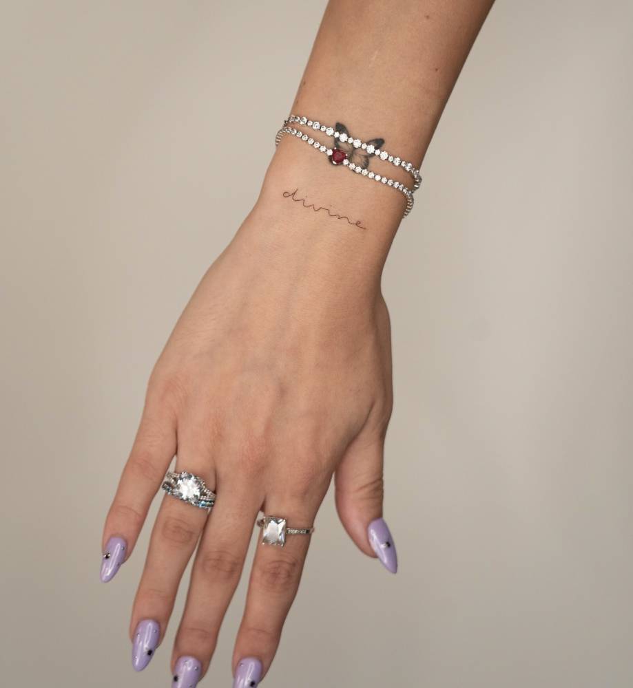 Lettering tattoo of the word divine handwritten on the wrist.