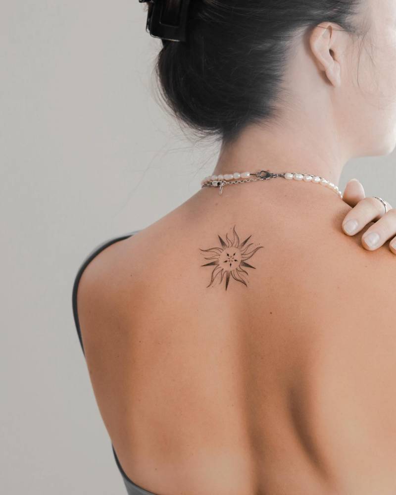 Sun tattoo located on the upper back, illustrative style.