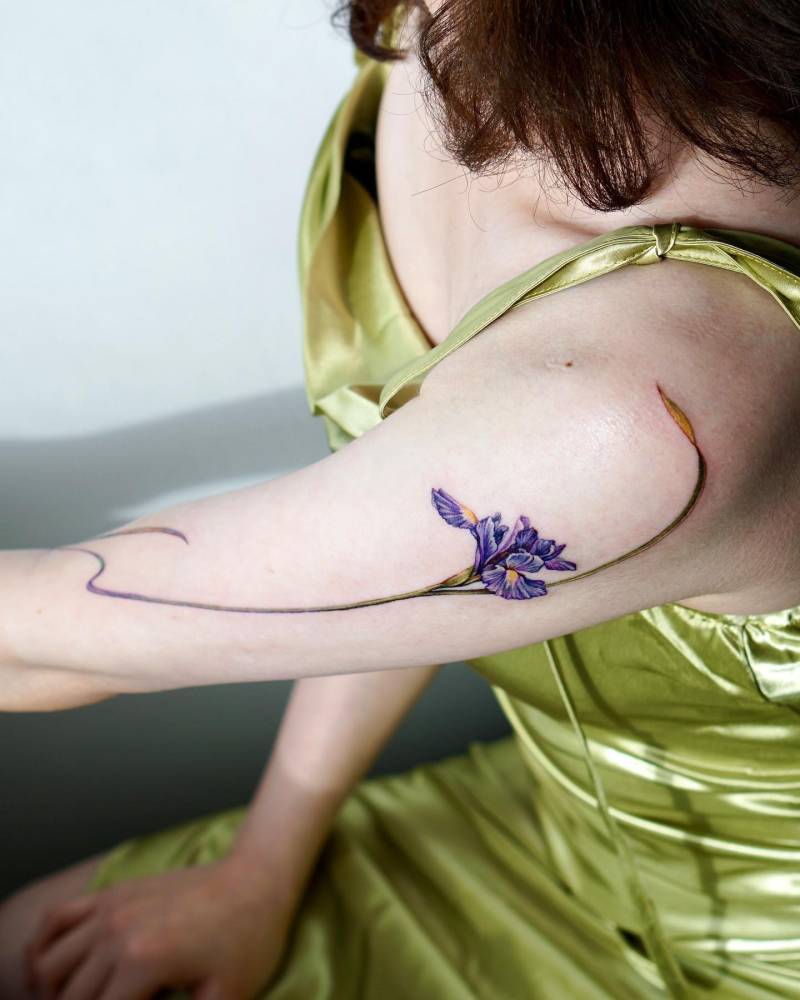 Watercolor style iris flower tattoo located on the upper arm.